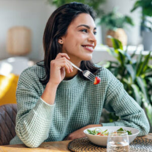 Portrait of beautiful smiling woman eating healthy salad at home.