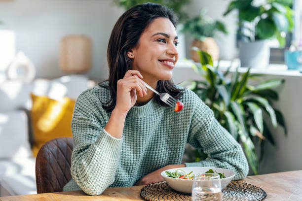 Portrait of beautiful smiling woman eating healthy salad at home.